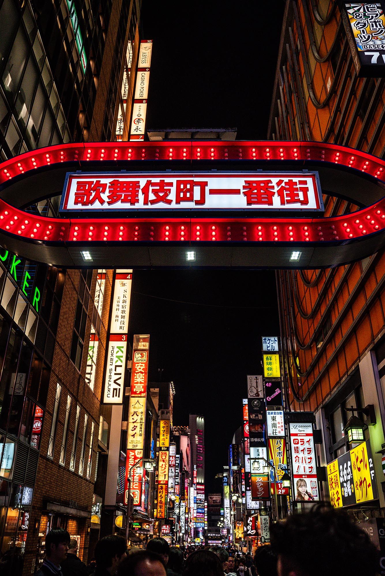 Bright neon signs and red LED lights illuminate a bustling nightlife district in Japan's Kabukicho entertainment area.
