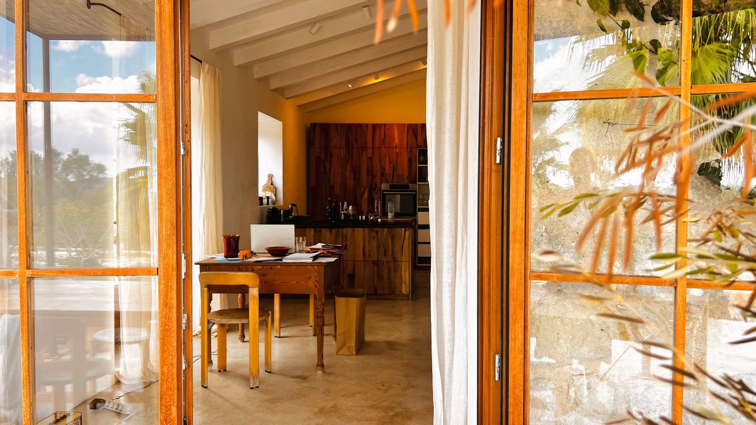 Bright sunlit dining room with wooden furniture and large windows overlooking a garden.