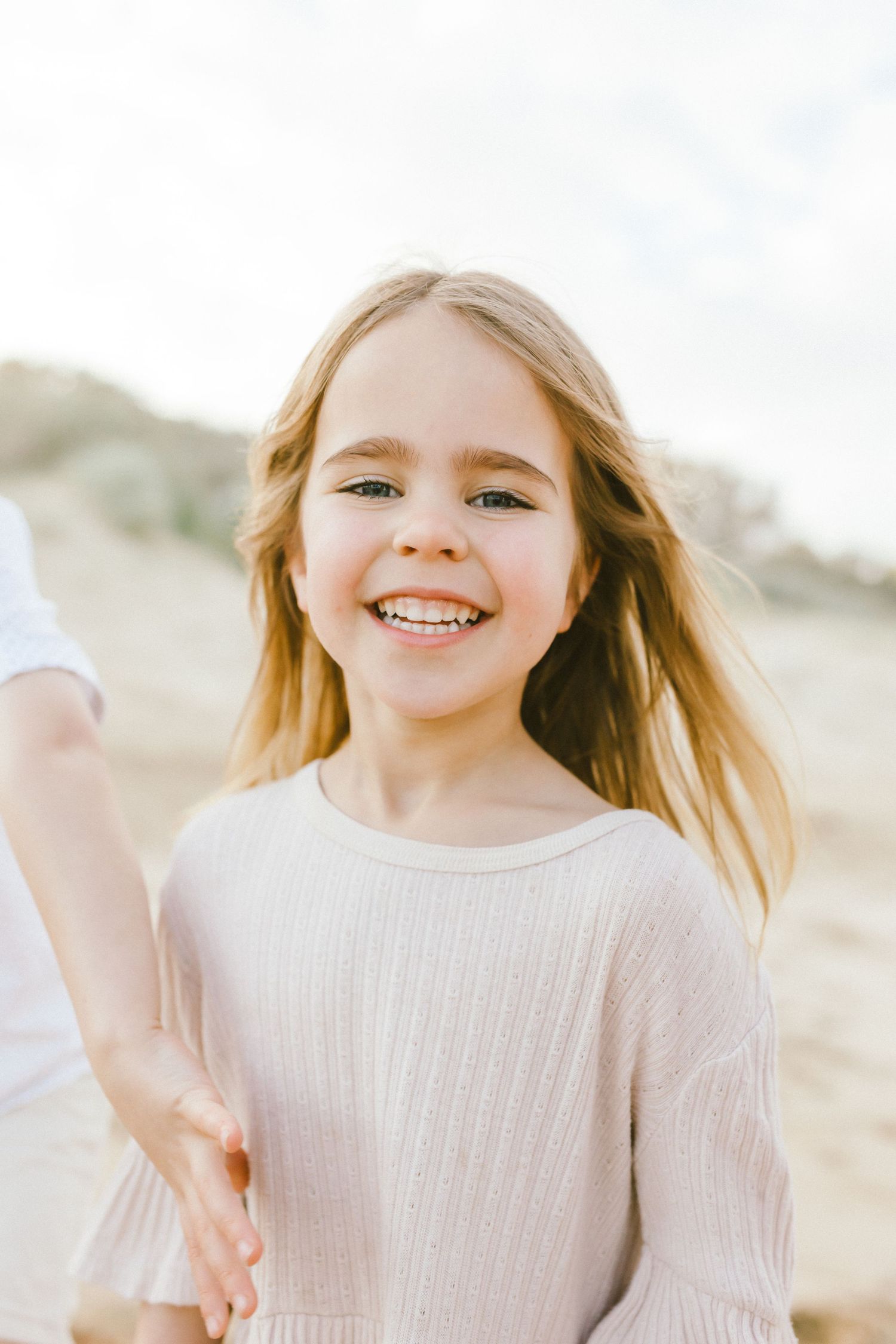 A young child wearing a cream sweater smiles and plays outdoors in natural light.
