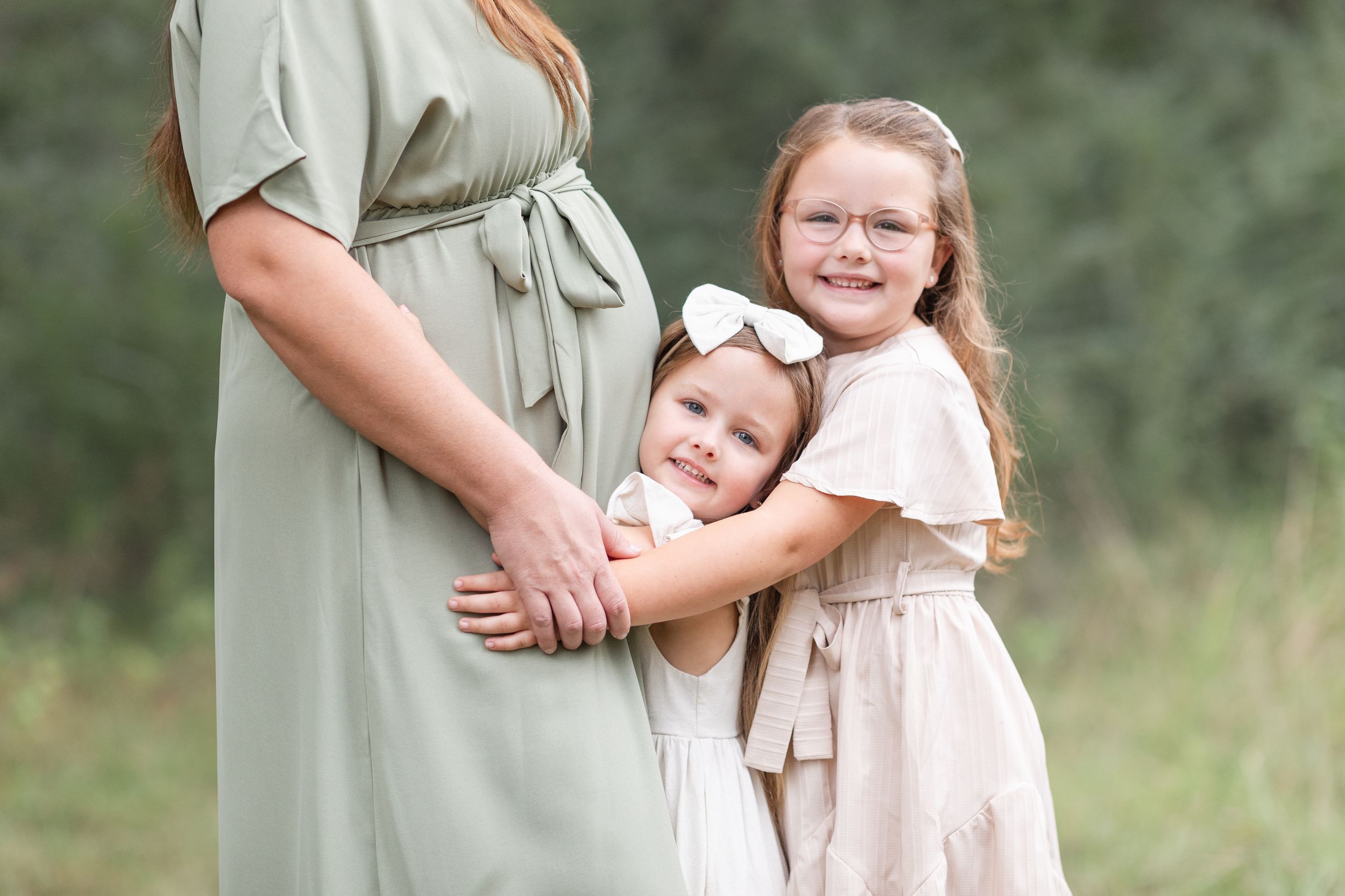 Tender family moment captured in soft lighting among trees and grass.