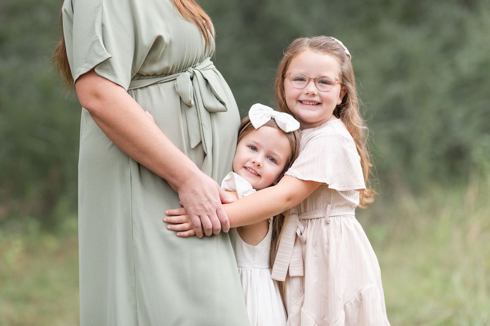 Tender family moment captured in soft lighting among trees and grass.