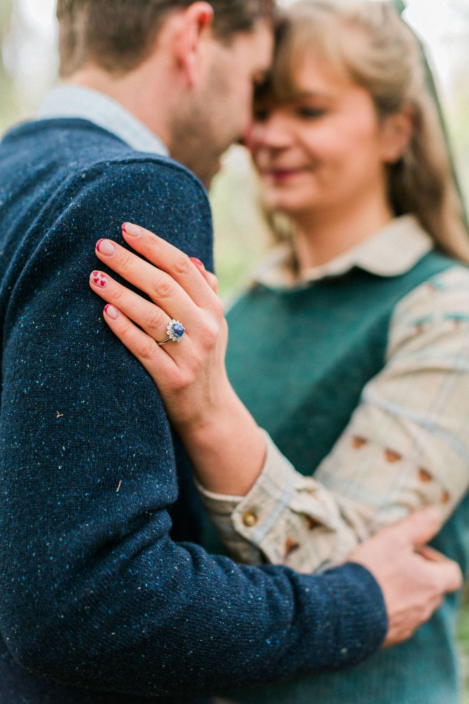 Close-up of an engagement ring on a hand resting against a navy sweater during an intimate woodland location. Hayley Elizabeth Photography.