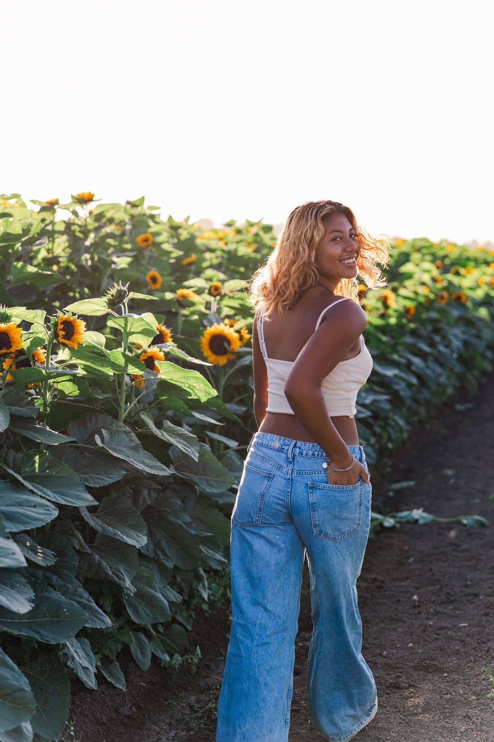 Casual summer style portrait in sunflower field wearing white top and relaxed fit jeans.