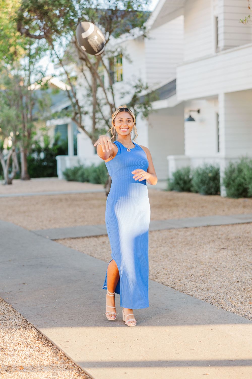 Woman in blue dress poses playfully on sandy outdoor path near white buildings.