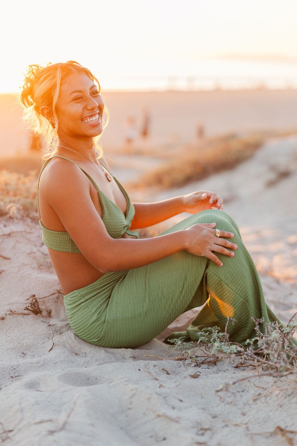 Person in green dress relaxes on sandy beach during sunset.