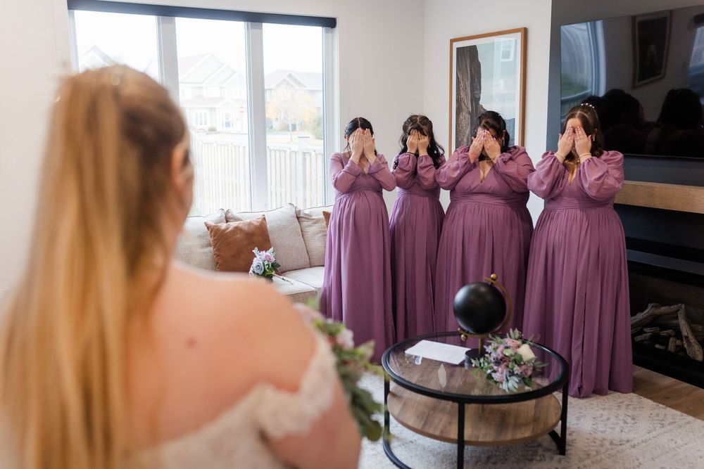 A wedding party gets ready in a bright room with bridesmaids wearing dusty rose colored dresses.