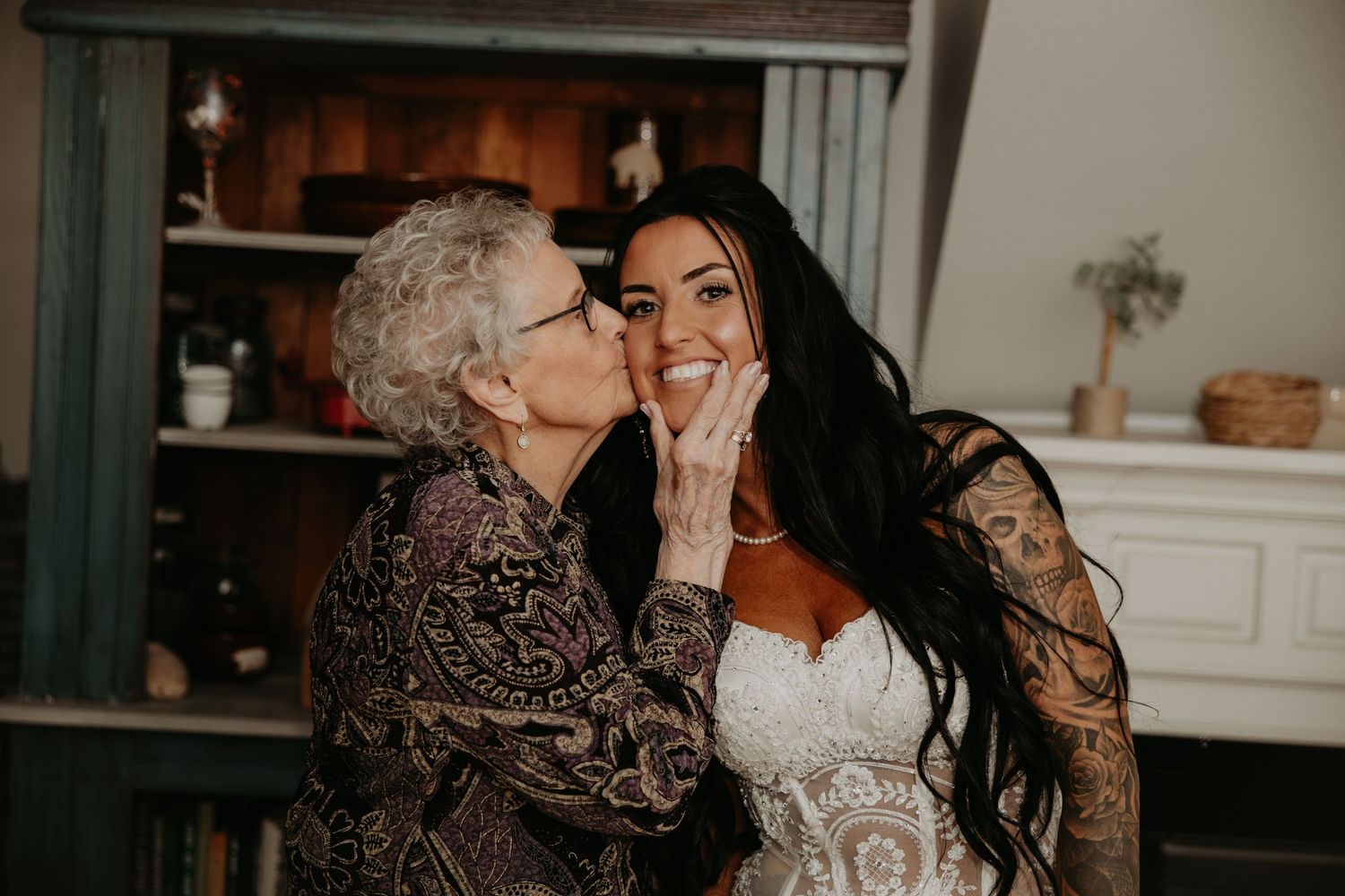 A tender moment shared between a bride in white lace and an elderly woman in a patterned dress.