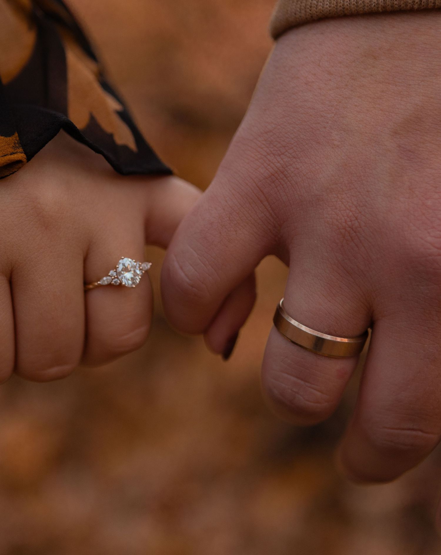 A close-up view of hands wearing wedding rings against a warm brown background.