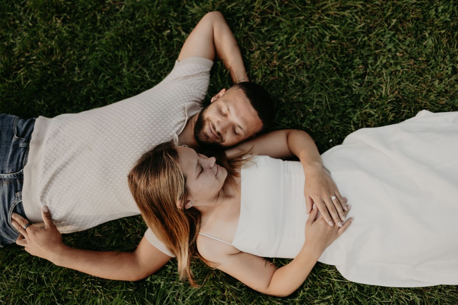 A couple lying on grass reading together in casual summer outfits.