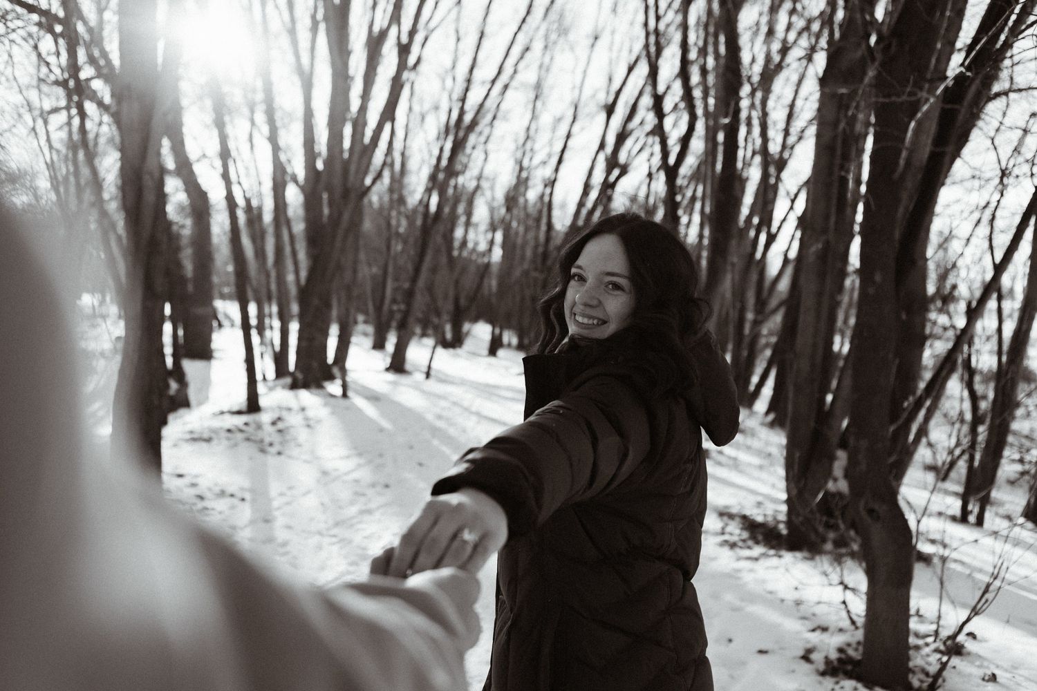 A snowy winter forest path winds through bare trees with a person walking in the distance.