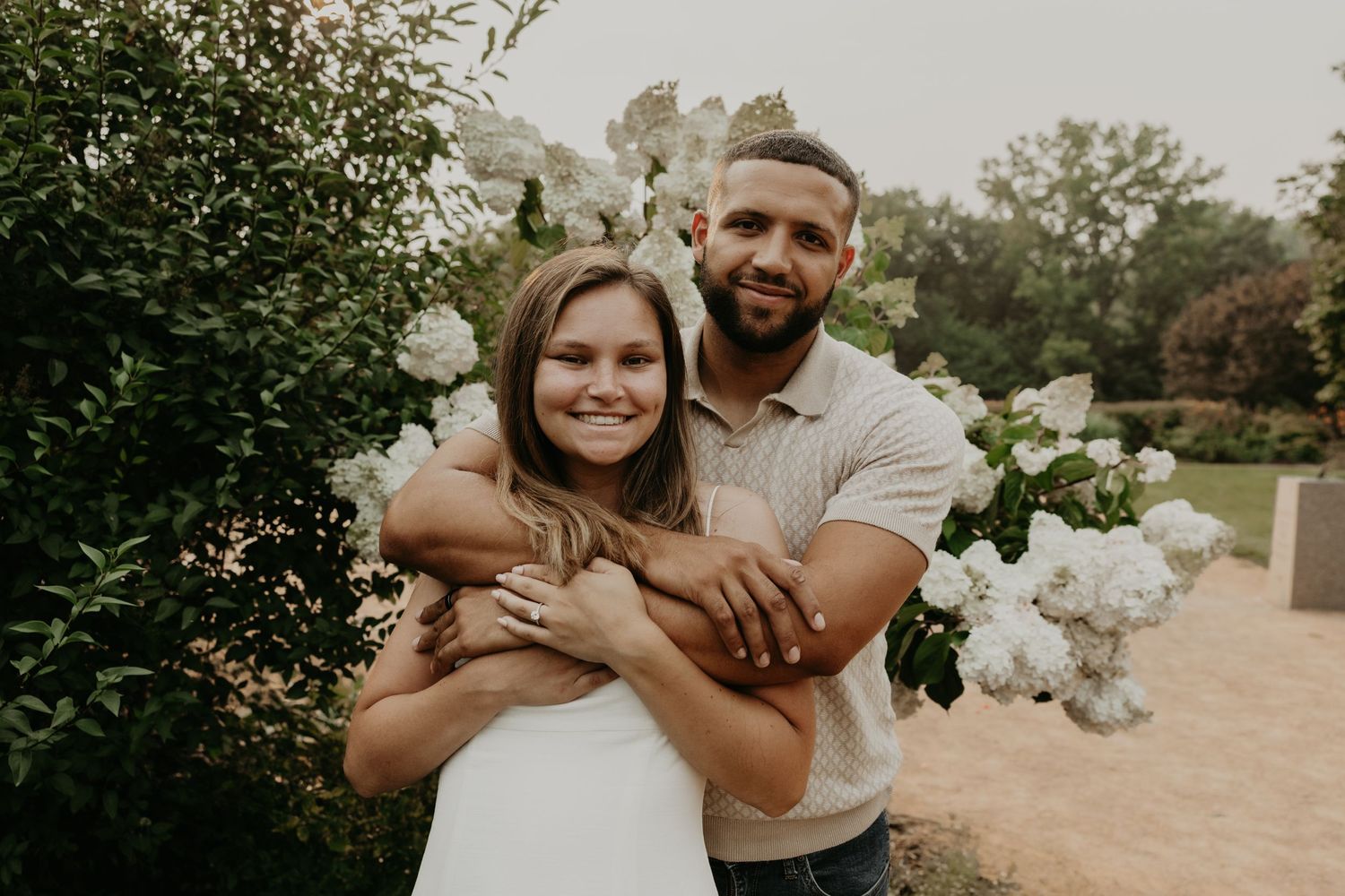 A romantic embrace among white flowering bushes in a garden setting.