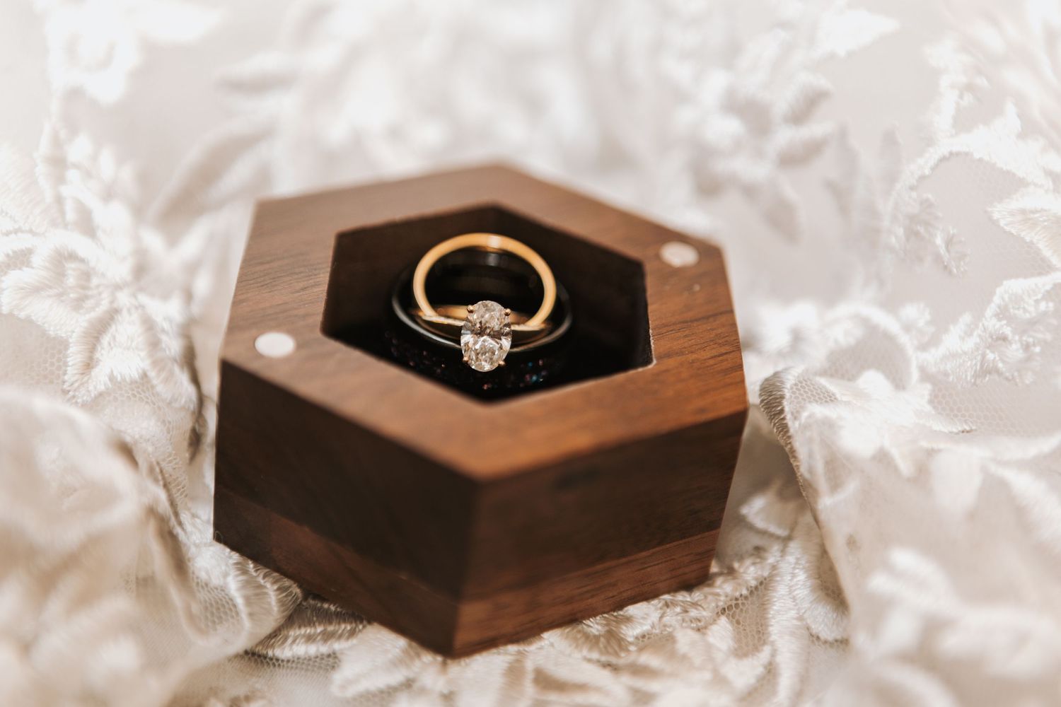 Close-up shots of wedding rings displayed in wooden boxes on white fabric.