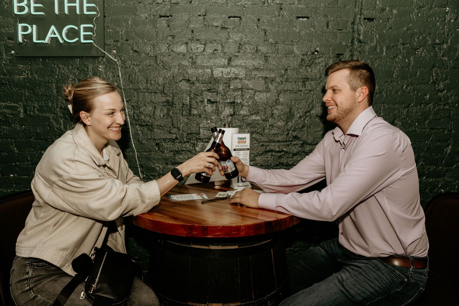 People sitting at a dark table against an exposed brick wall in a dimly lit space.