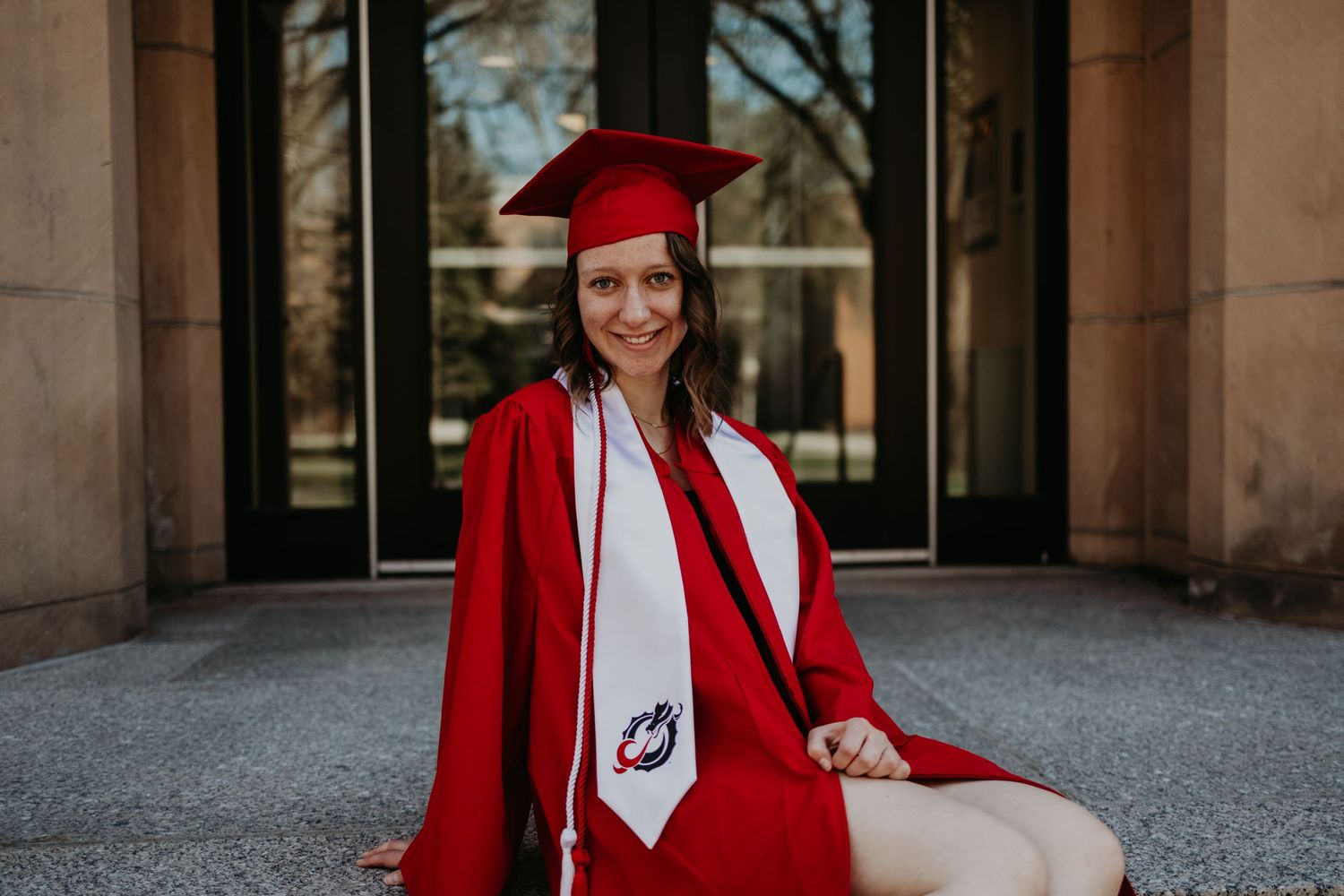 A graduation photoshoot featuring bright red academic regalia against stone architecture.