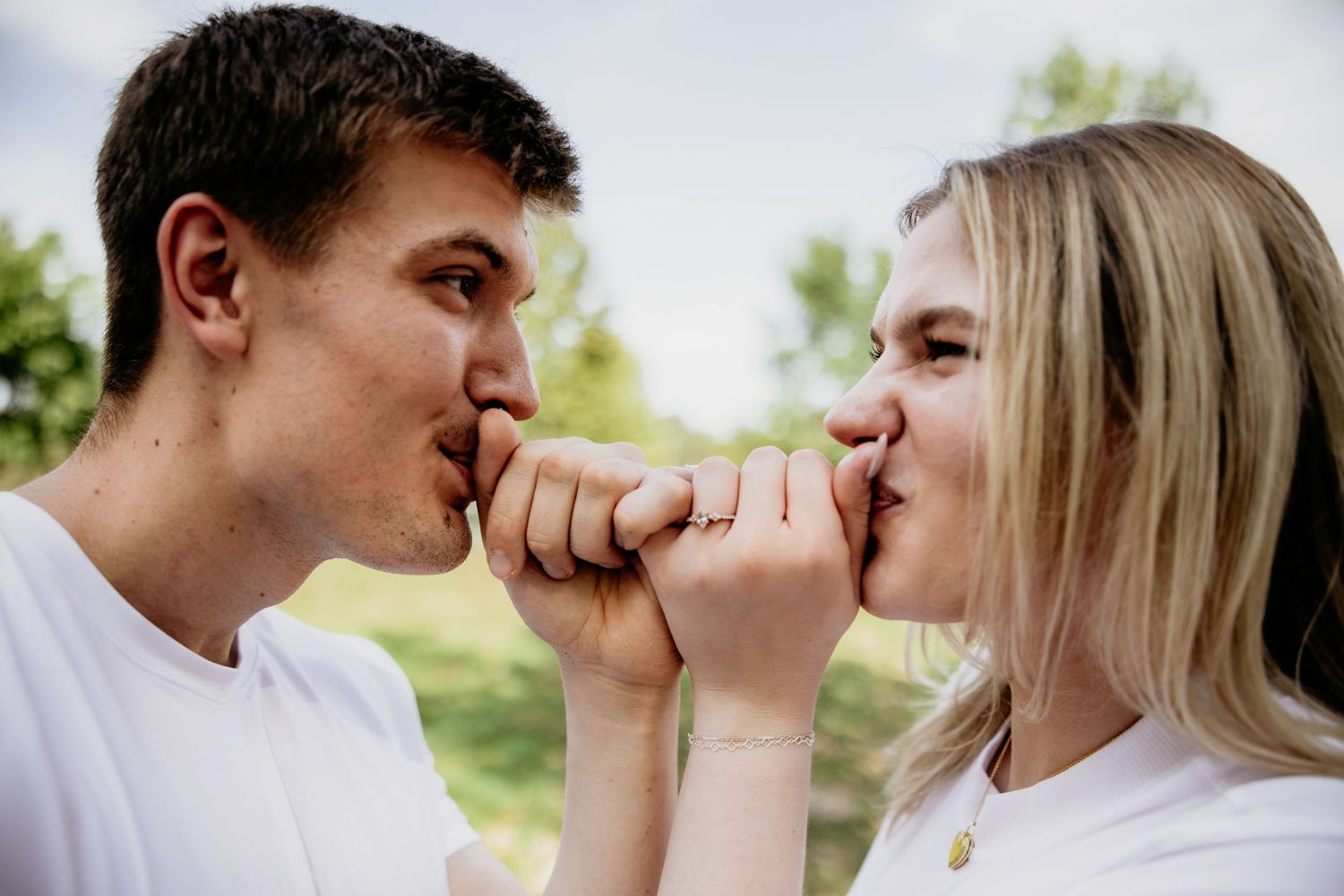 Two people in white shirts playfully touch noses while sharing an intimate moment outdoors.