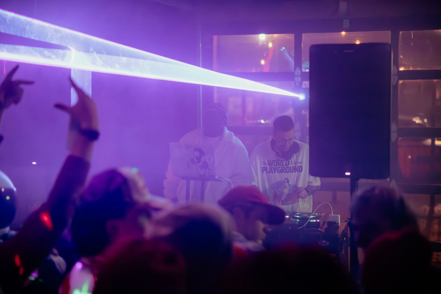 Purple neon lights illuminate a dark nightclub atmosphere with silhouettes of people dancing and socializing.