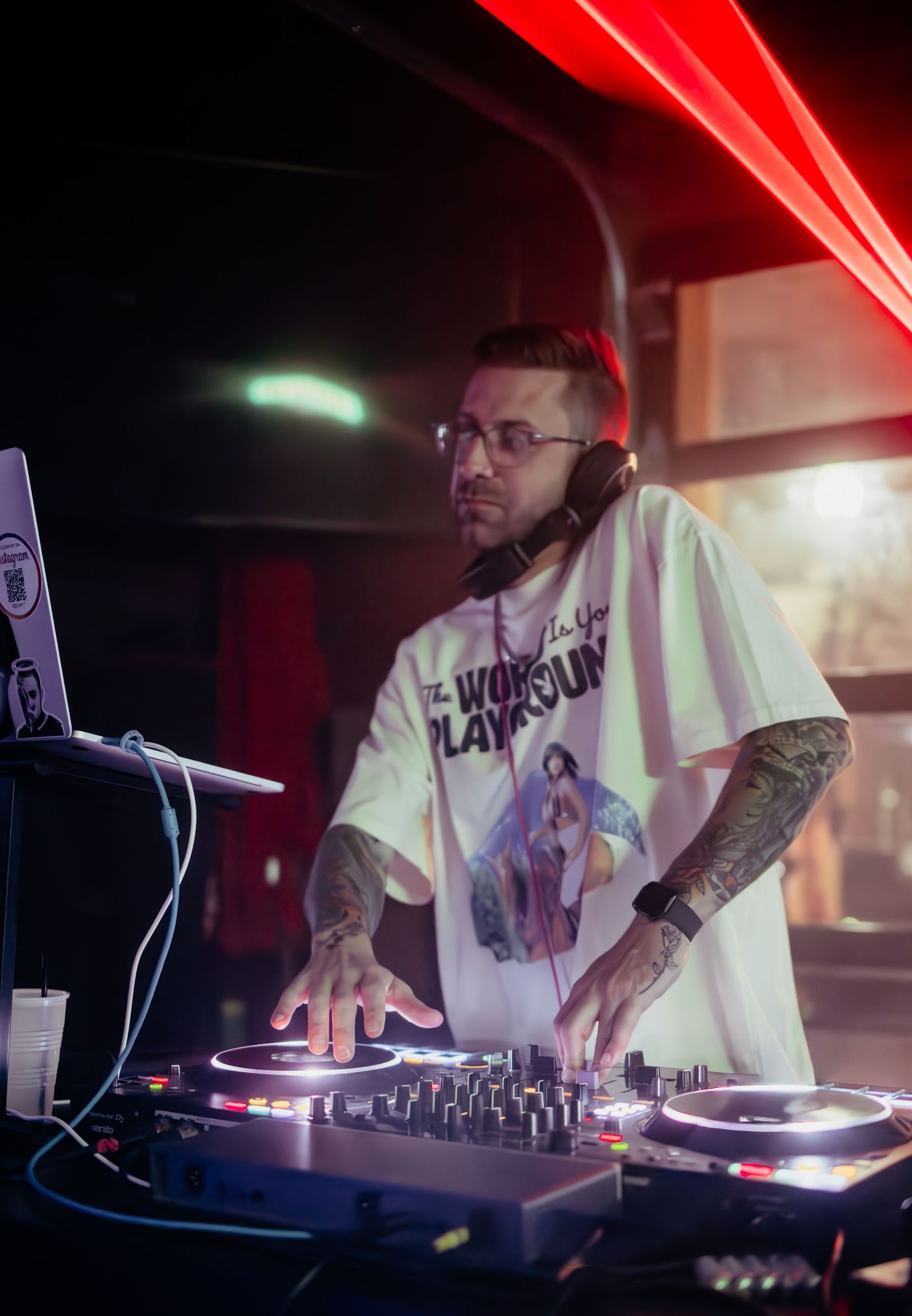 DJ performs with turntables and mixer under dramatic red lighting at a nightclub.