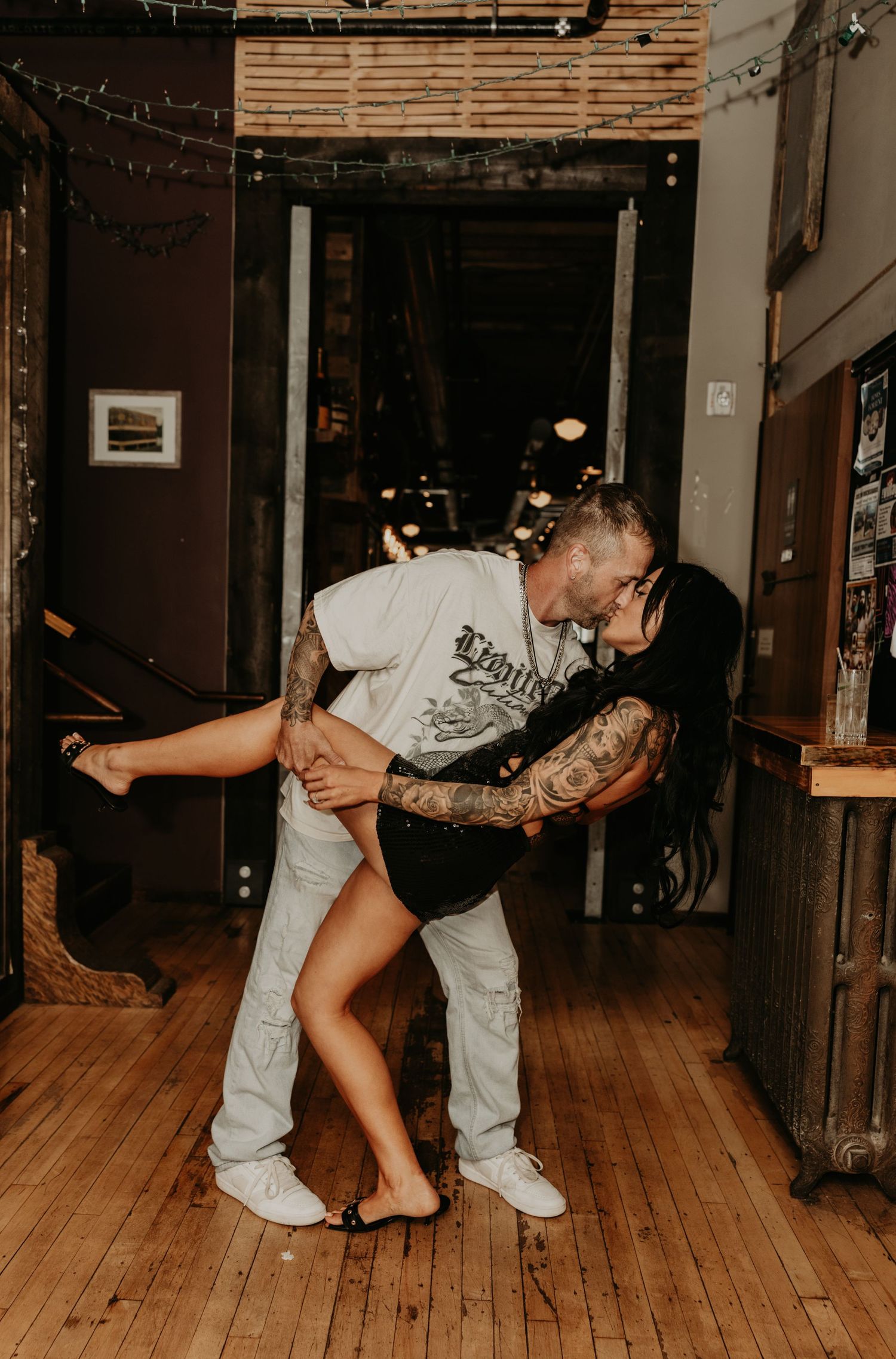 Playful dance sequence on a rustic wooden floor with string lights overhead.
