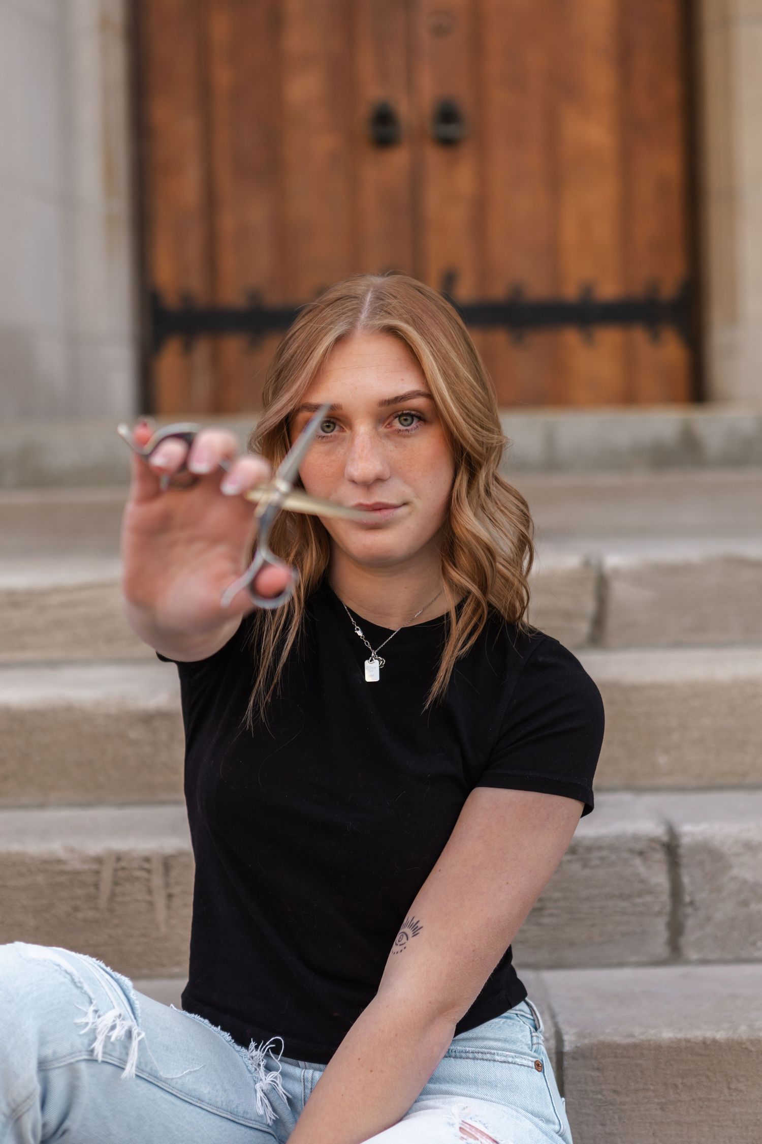 A person in a black t-shirt and light jeans sits on concrete steps in a casual outdoor branding photography.