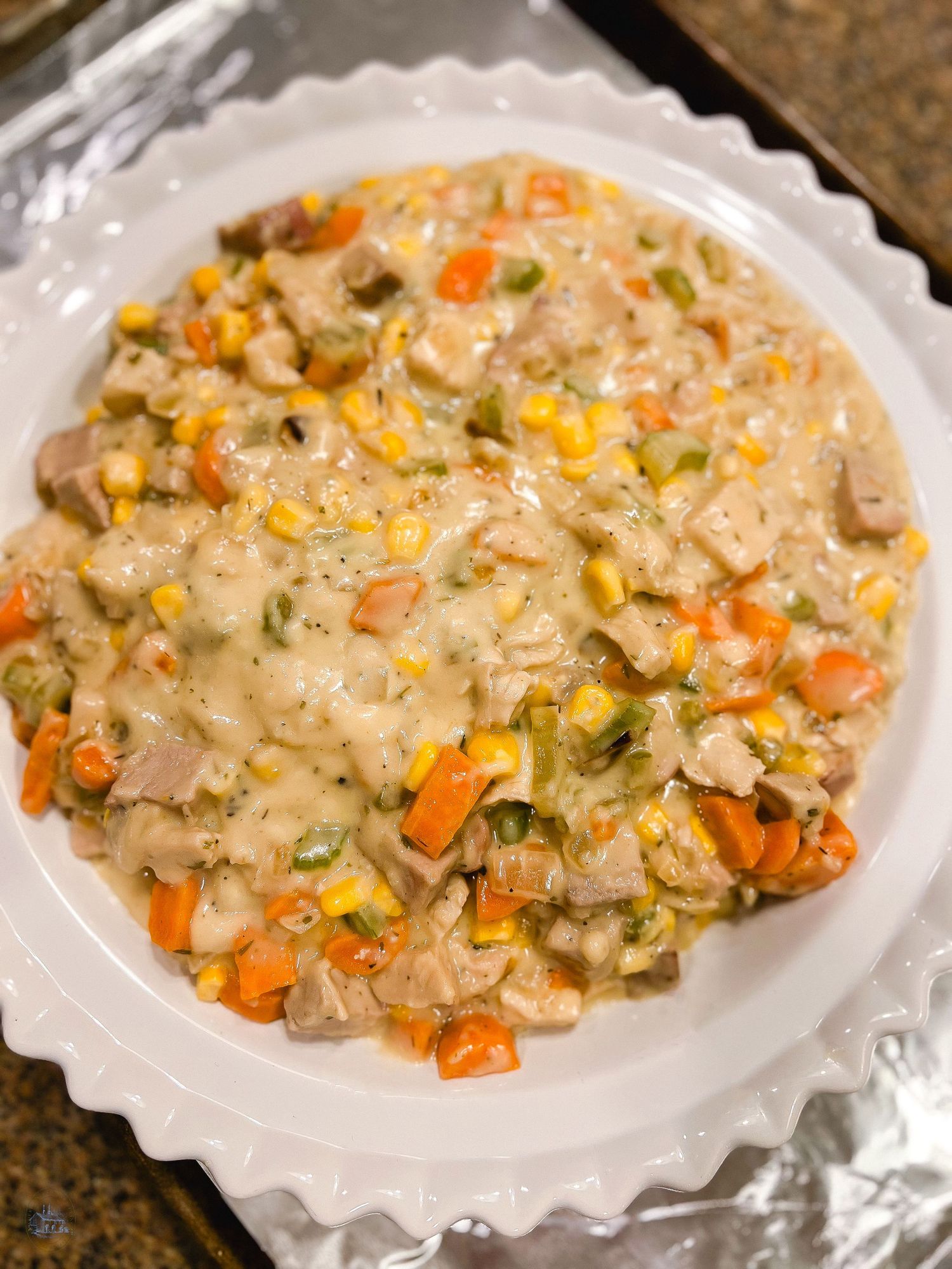 Creamy chicken pot pie filling with carrots and vegetables in a white dish.