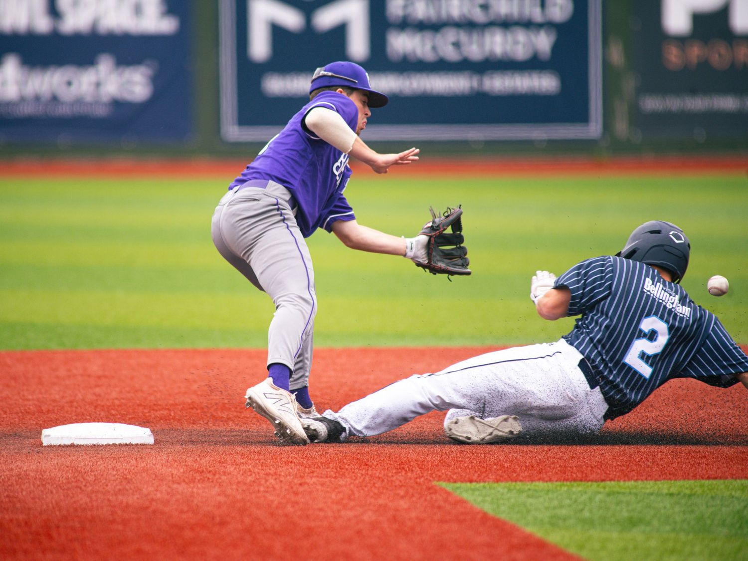 Baseball player in purple jersey attempts to tag sliding baserunner wearing pinstripes during action play at second base.