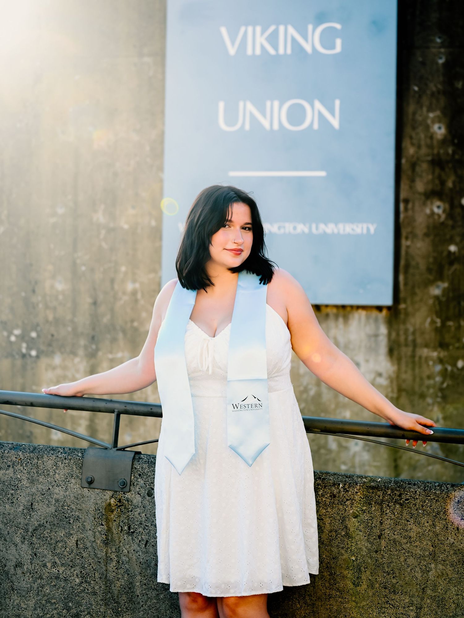 Person in white dress poses confidently against concrete wall with Viking Union sign.