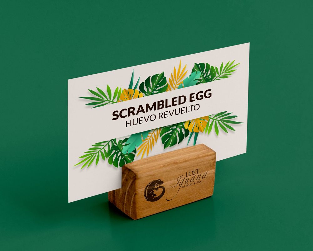 Wooden holder displaying menu card with tropical leaf design against green background.