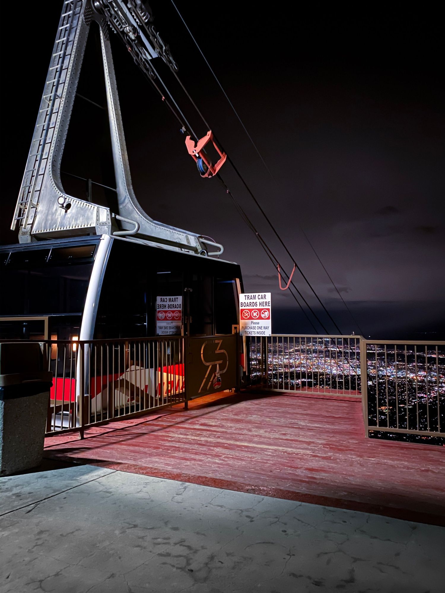 A red ski lift chair silhouetted against dark night sky with illuminated platform below.