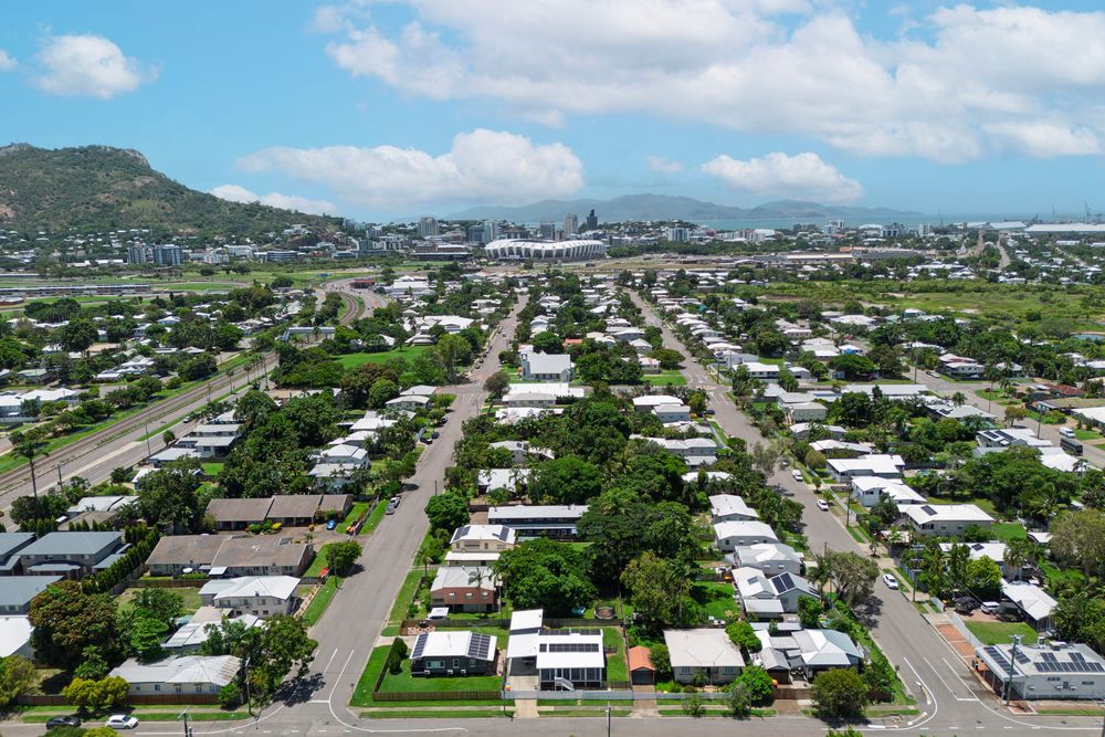 Aerial panoramic view of a coastal residential neighborhood with mountains in the background under blue skies.
