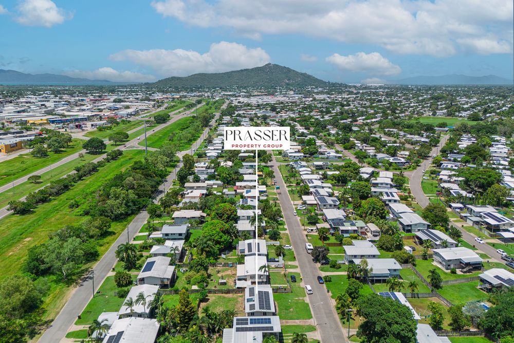 Aerial panoramic view of a coastal residential neighborhood with mountain backdrop and lush greenery.