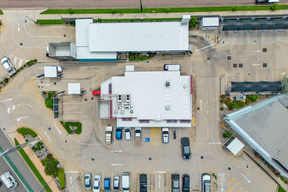 Aerial drone view of a commercial shopping center with parked cars and retail buildings in a suburban area.