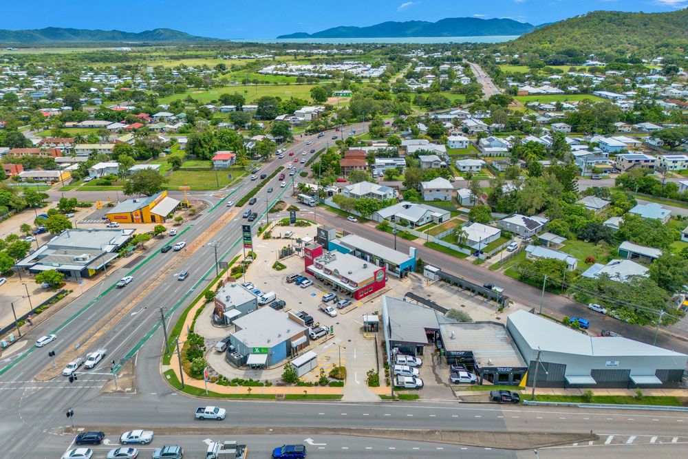 Aerial view of a busy intersection in a coastal town with mountains in the background and commercial buildings below.