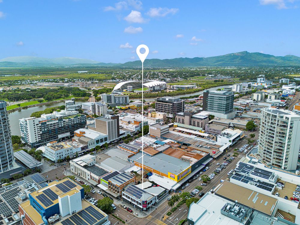 Aerial view of downtown Cairns city skyline with modern buildings and mountains in the background on a sunny day.