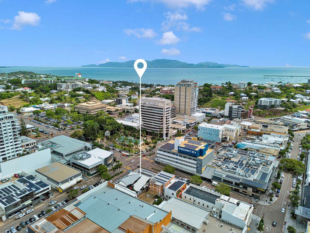 Aerial view of Townsville city center with Castle Hill and Magnetic Island visible in the background across blue waters.