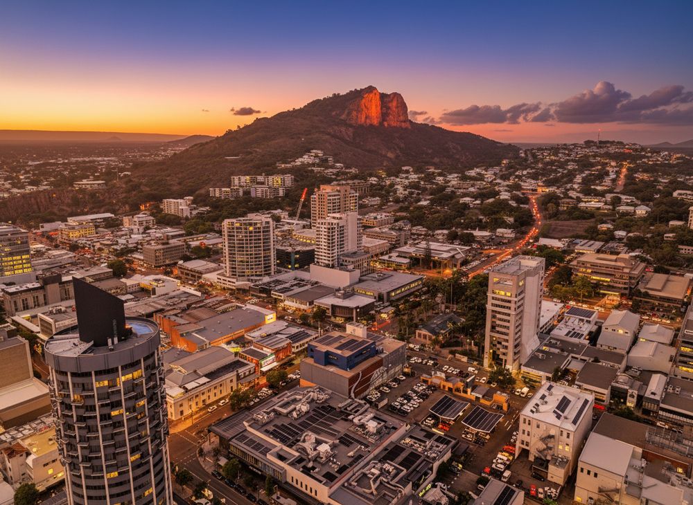 Panoramic aerial view of Honolulu city skyline at sunset with mountains and orange sky in the background.