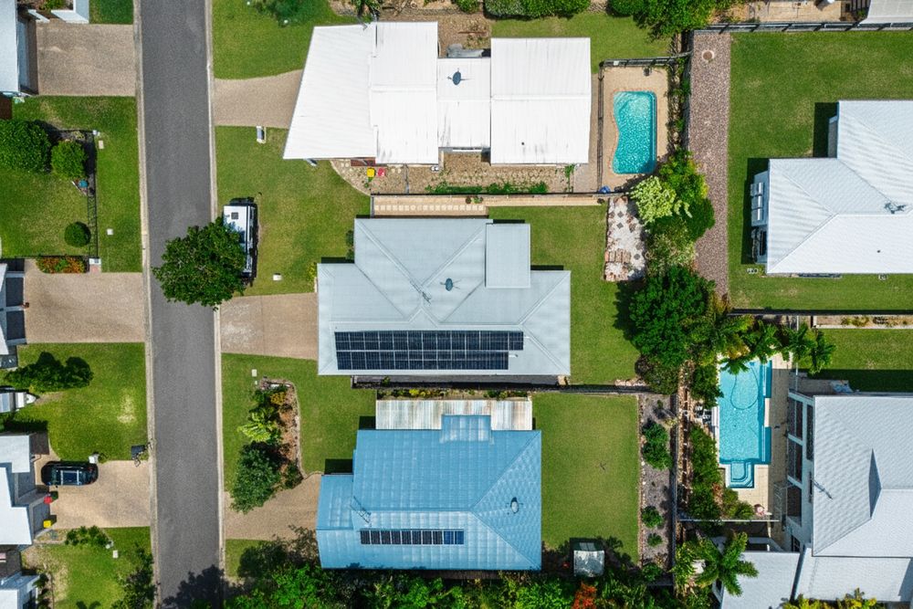 Aerial drone view of residential neighborhood with houses, green lawns, and streets on a sunny day.
