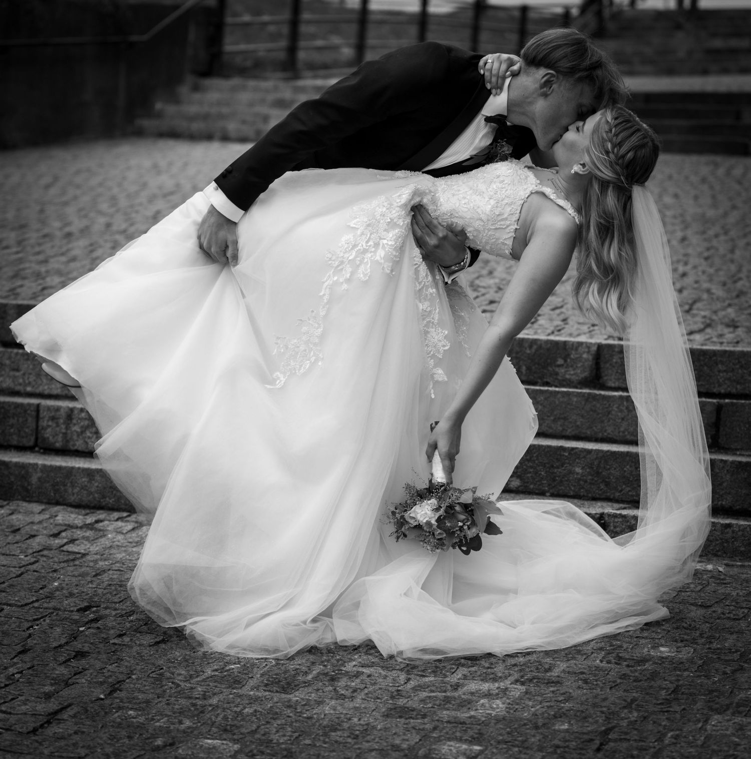 Black and white romantic photo of groom dipping bride for a kiss on stone steps.