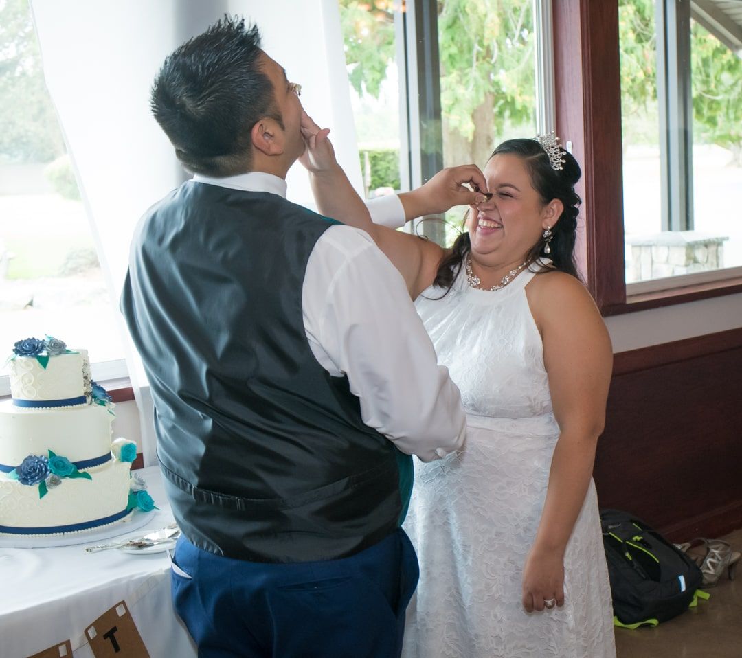 Bride and groom at High Cedars Golf Course in Orting, WA during cake cutting.  Both are sticking cake onto each other's noses and giggling.