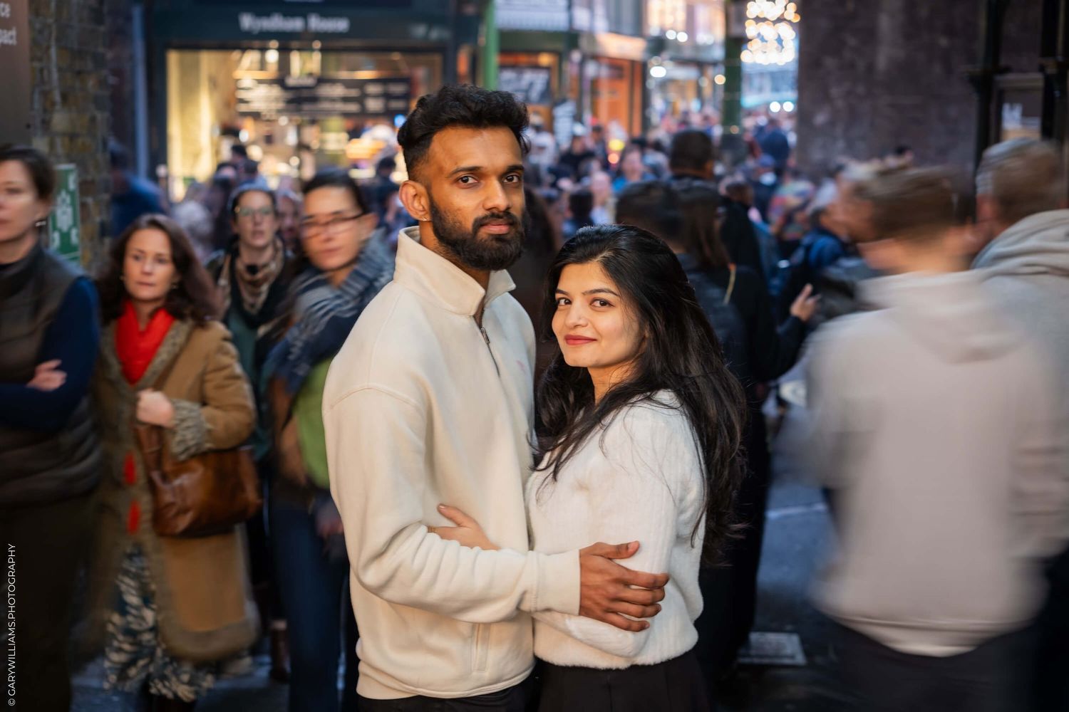 A couple embraces on a busy London street filled with people.