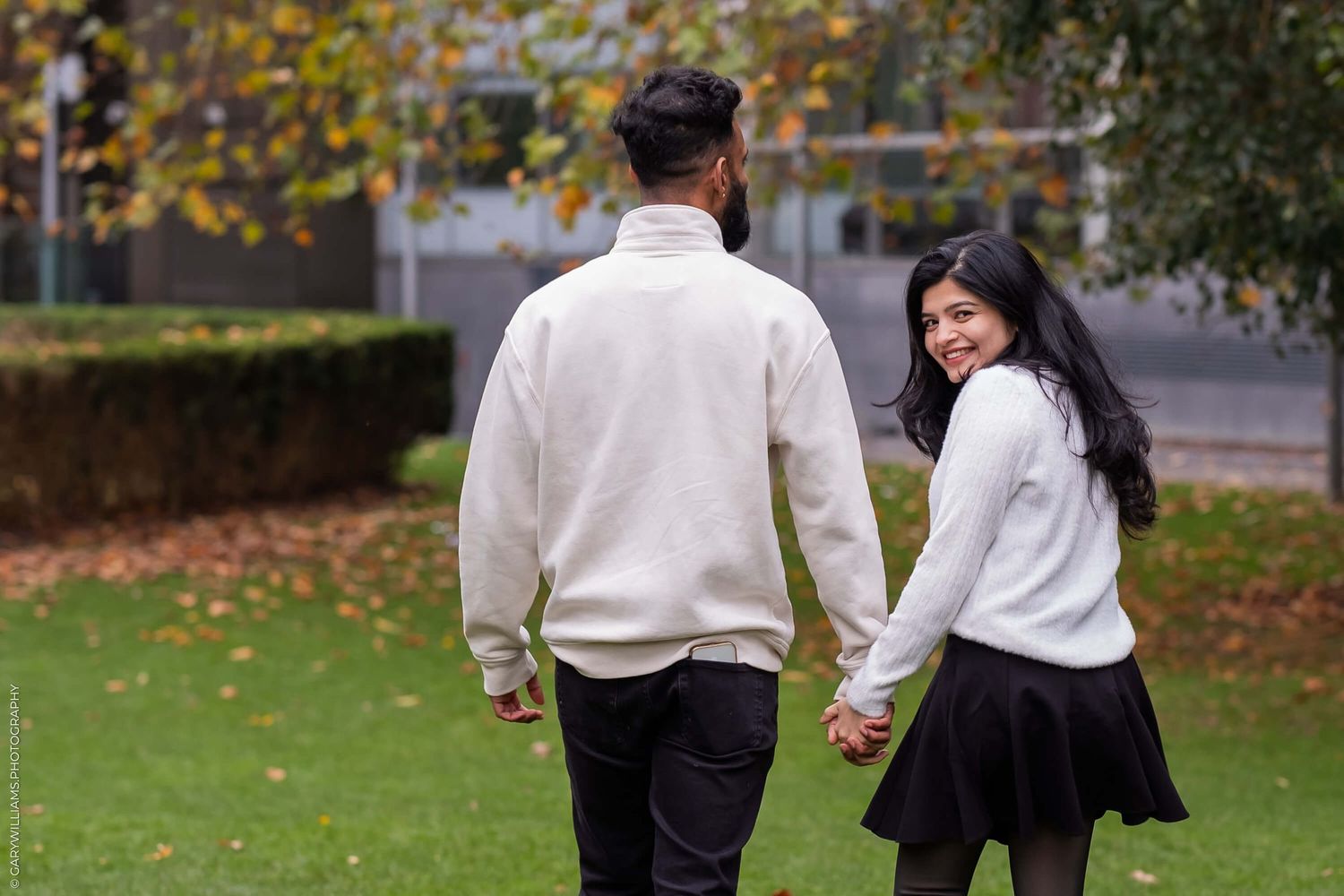 A couple in matching white sweaters walking through an autumn park.