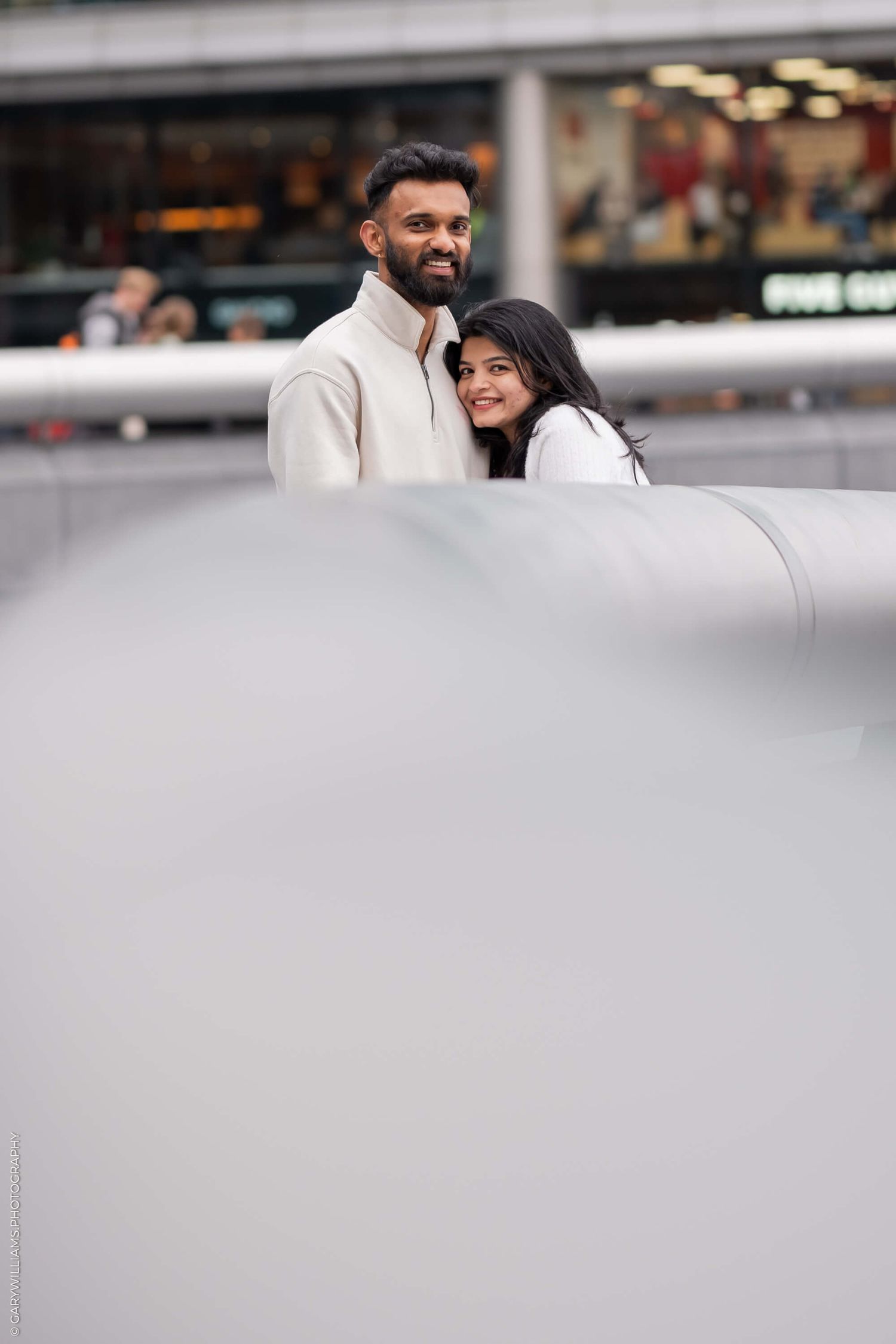 A couple sharing a tender moment together on an urban street with storefronts in the background.