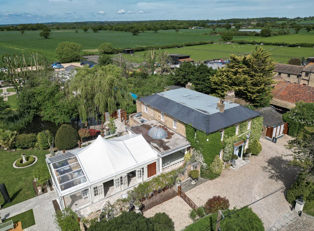 Aerial view of a countryside property with white and gray buildings surrounded by green fields.