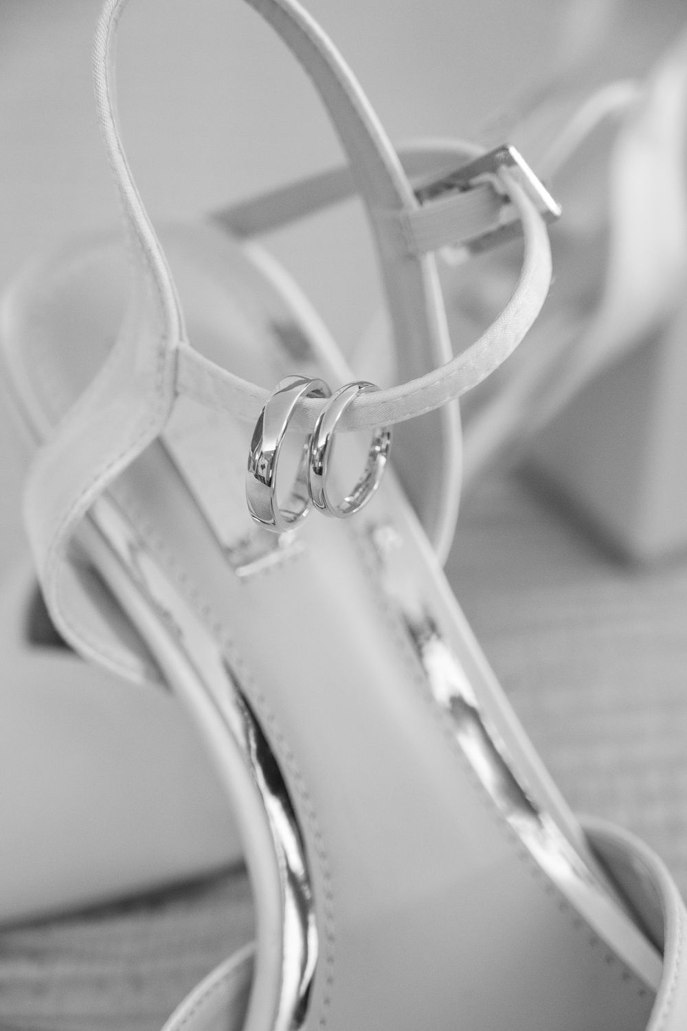 Wedding rings placed delicately on a white high-heeled shoe strap.