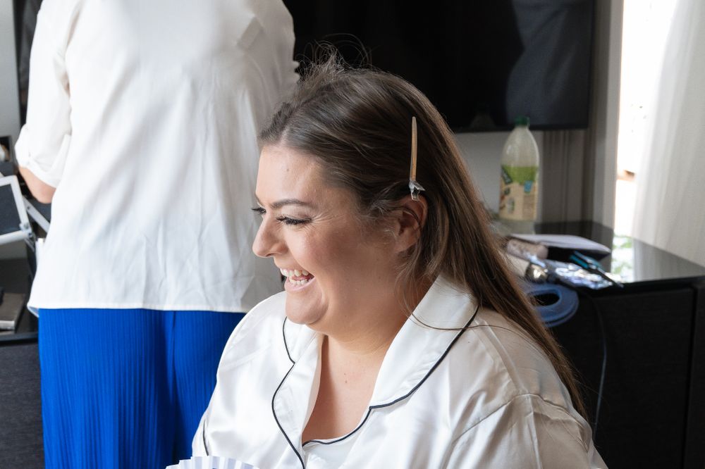A woman in white loungewear smiles while sitting and looking down during a relaxed moment.