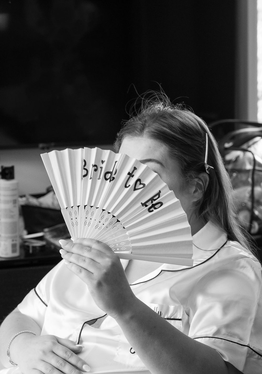 Person in white holds up a decorative fan while smiling and laughing.