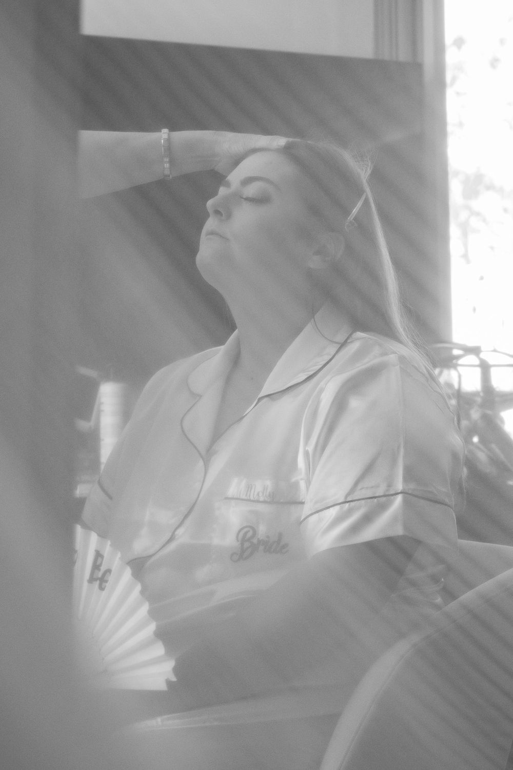 Artistic black and white photo of someone resting with a fan in a dreamy pose.
