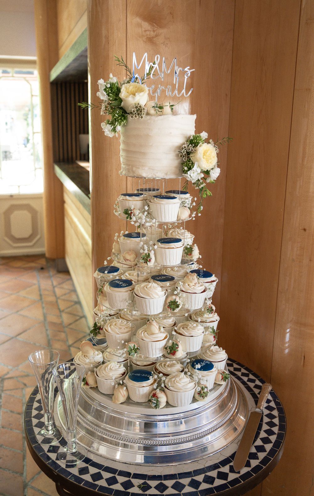 Tiered wedding cake display with white frosting, blue accents and floral decorations.
