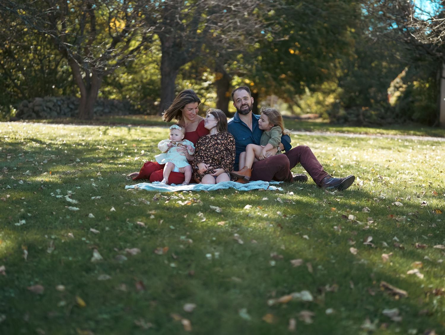 Group relaxing on blankets under trees in a sunny park setting.
