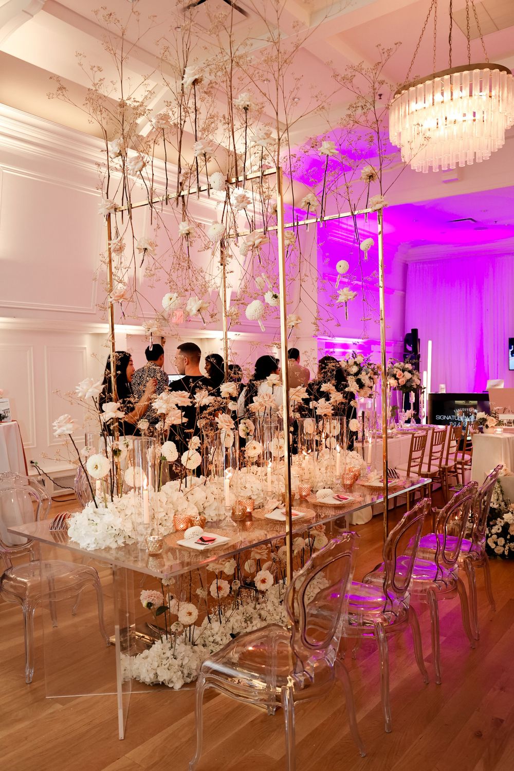 Elegant wedding reception table with crystal chairs and floral centerpieces illuminated by purple lighting.