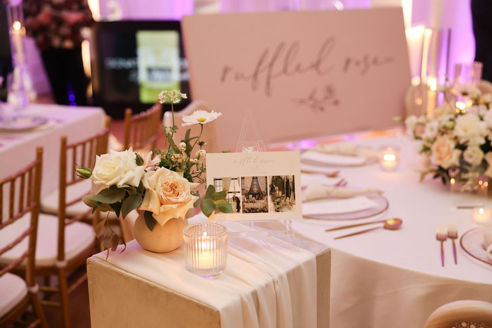 Romantic table setting with pink name card, roses, and candlelight at an elegant wedding reception.